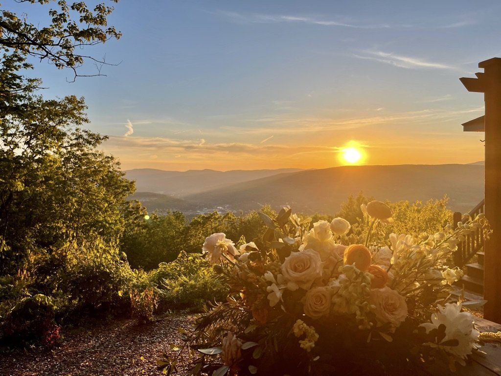 Mahican Cabin - Golden sunset over distant hills, illuminating a large, lush floral arrangement in the foreground.