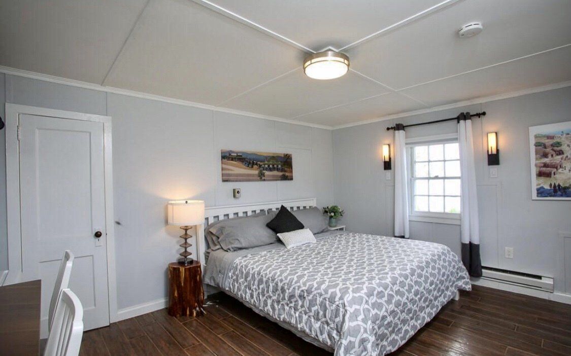 A bedroom with light gray walls, a bed featuring a patterned comforter, bedside lamp, and white door.