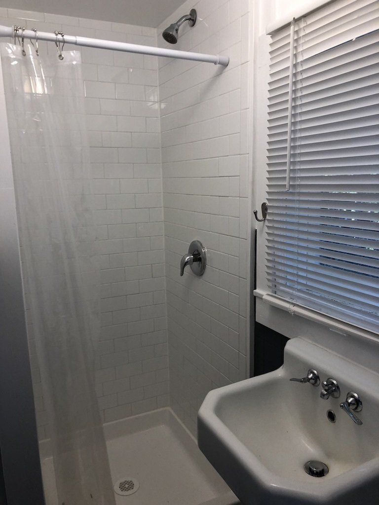 A small bathroom featuring a white subway-tiled shower with a clear curtain, silver fixtures, and a white corner sink.