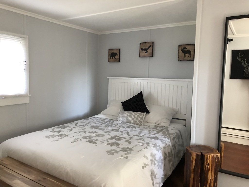A cozy bedroom with a white bed, floral bedding, a wood bed frame, three framed animal wall art pieces, and a floor mirror.