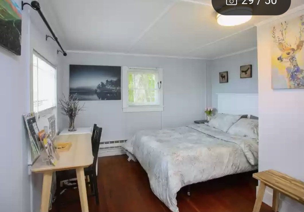 A bedroom with a queen bed, wooden floors, a desk with a chair, and wall art including a deer print.
