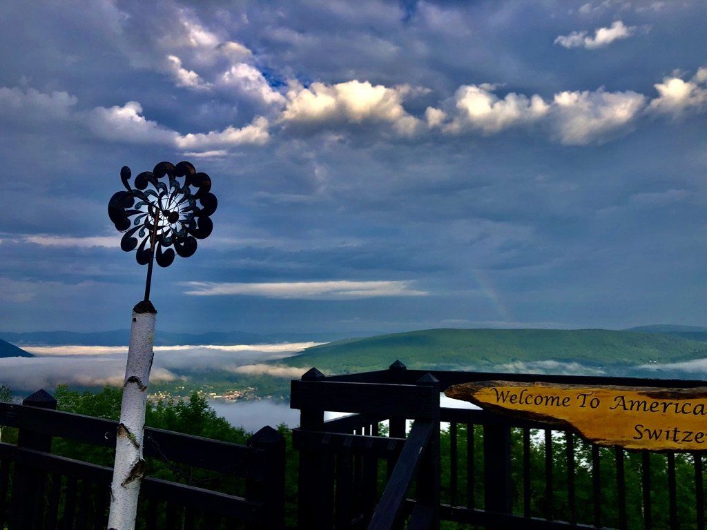 A view from a deck overlooking a valley filled with fog under a dramatic, cloudy sky, with a sign saying Switzerland.