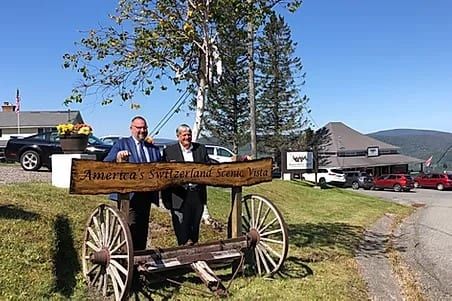 Two people stand behind a wagon-wheel sign reading