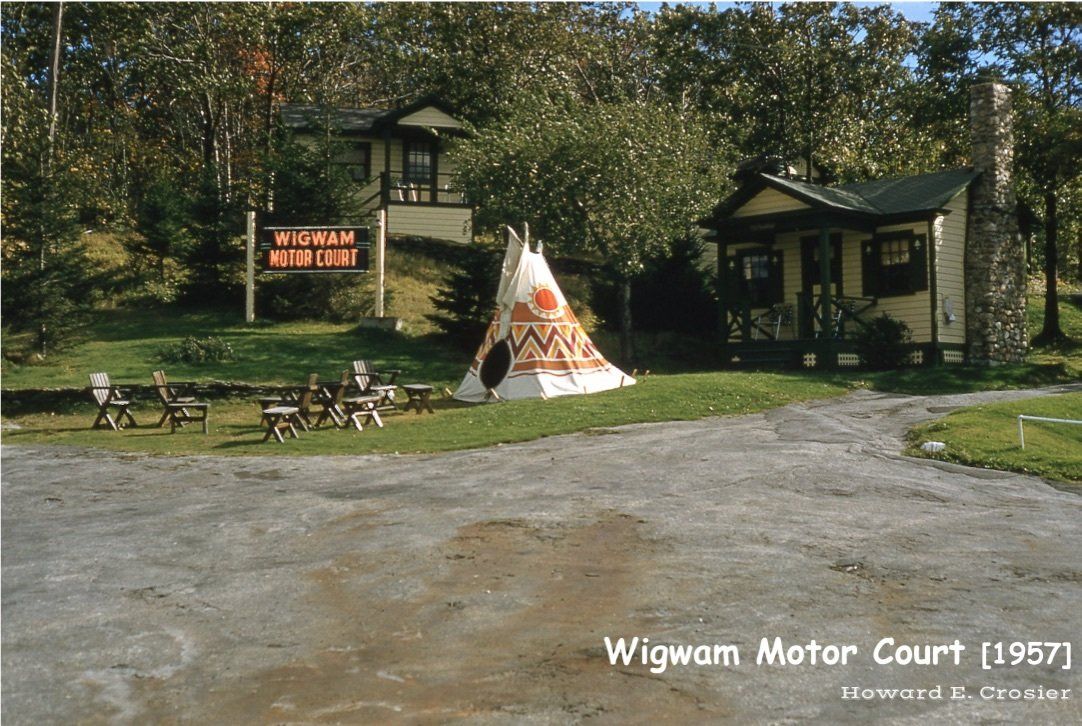 A 1957 photo of the Wigwam Motor Court showing a small cabin, a decorative teepee, and a sign on a grassy lawn.