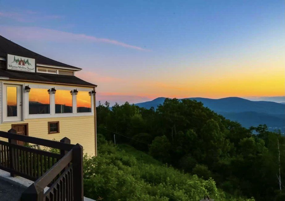A yellow building overlooking a lush green mountain landscape at sunset, with the sky reflected in the building's windows.