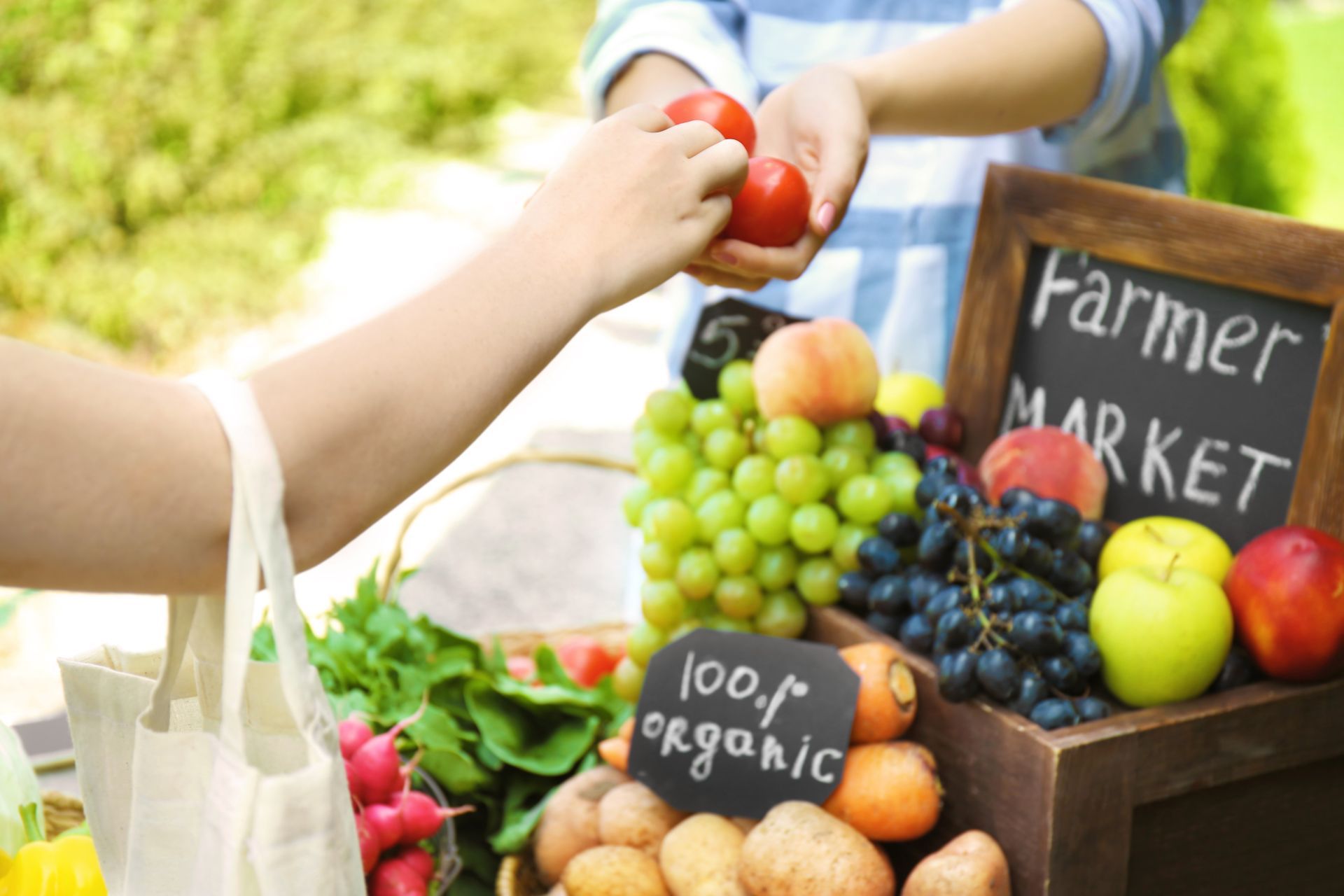 A person is holding a tomato at a farmers market.