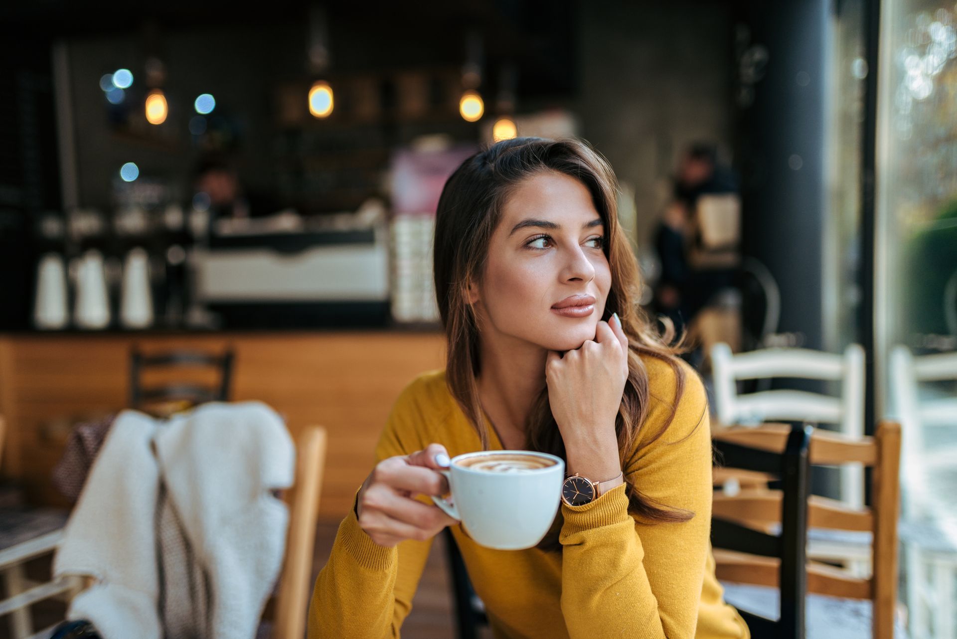 A woman is sitting at a table in a cafe holding a cup of coffee.