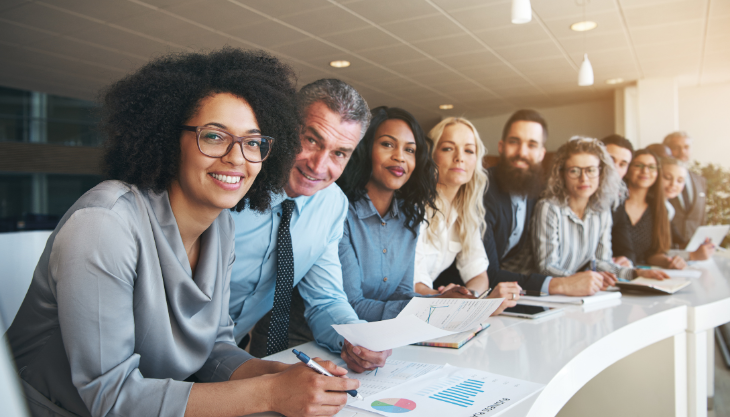 A diverse group of company leaders and staff sitting at a table and smiling, emphasizing the need for diverse management