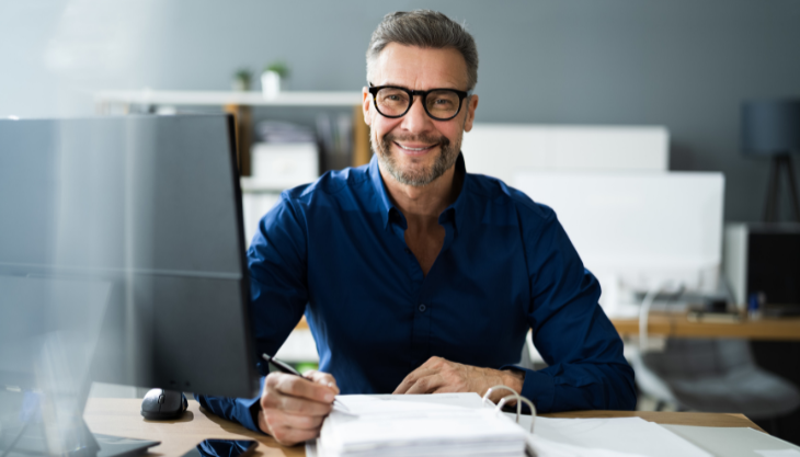 An expert on payroll taxes smiles confidently at the camera as he works on a client's payroll tax management tasks