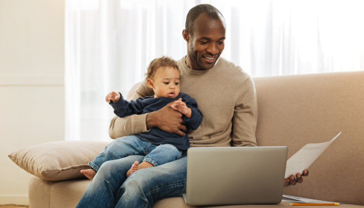 New father carrying his child while working in front of computer