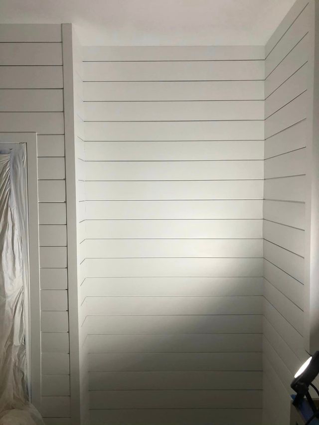 A room with white wood paneling and a light on the wall.