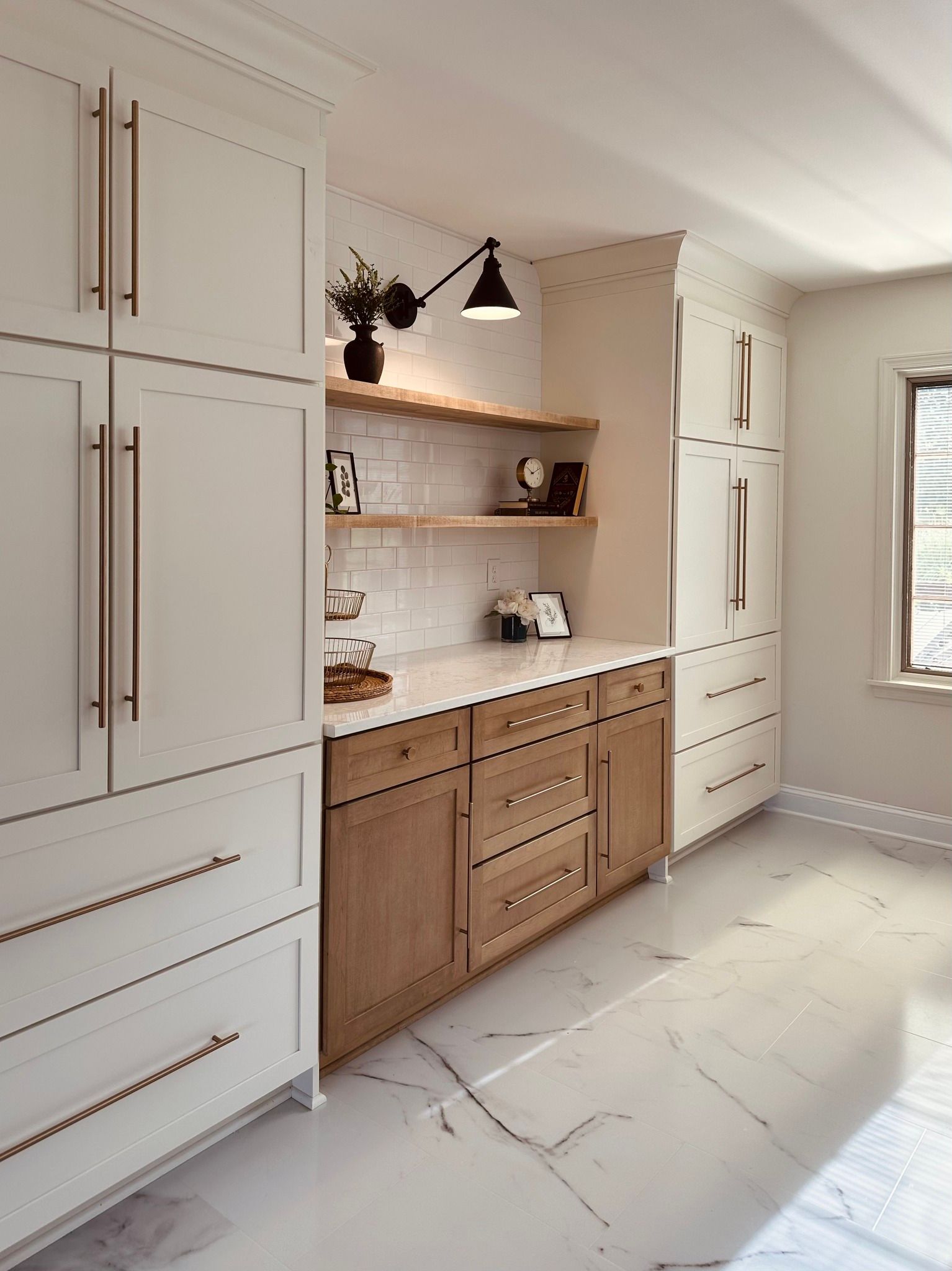 A kitchen with white cabinets and wooden cabinets and a marble floor.