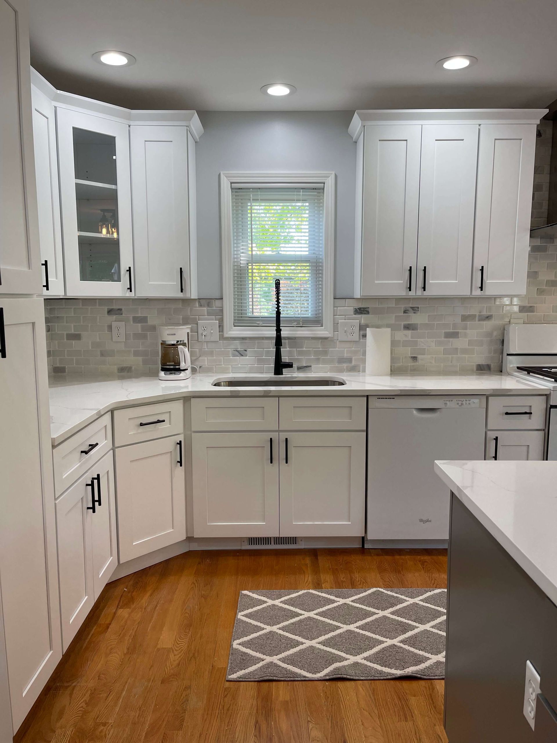 A kitchen with white cabinets , a sink , and a window.