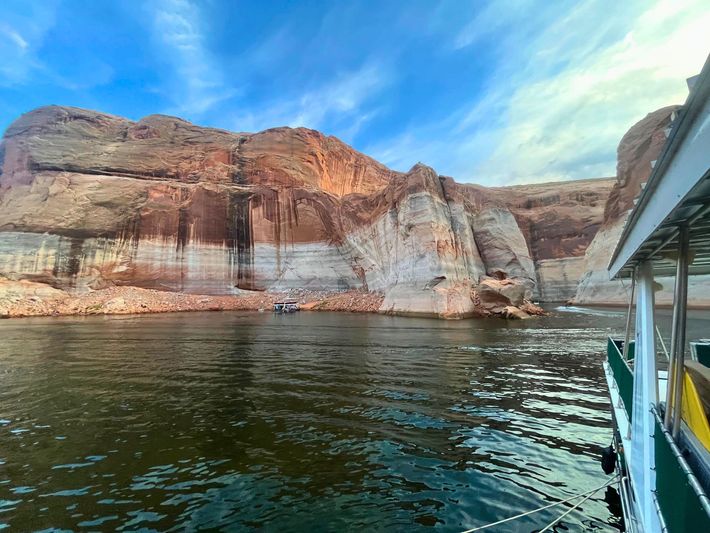 Rocky canyon cliffs beside calm water, viewed from a boat under a blue sky.