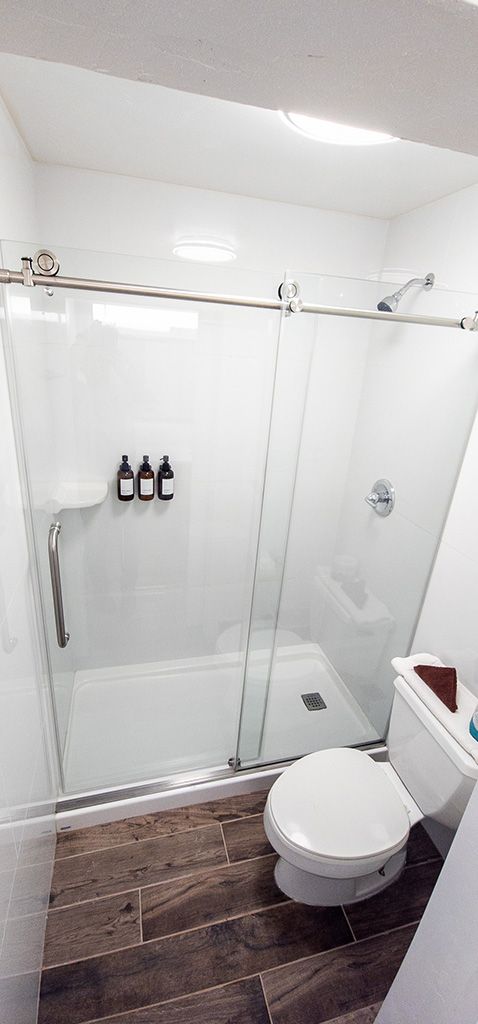 Small bathroom with glass shower enclosure, white toilet, and dark wood-look floor tiles