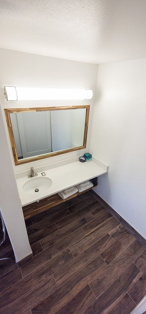 Small bathroom vanity with large mirror, white sink, wall light, and dark wood floor.