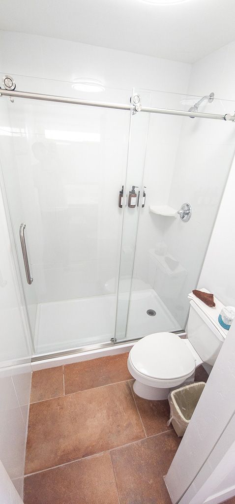 Small bathroom with white shower stall, toilet, and terracotta floor tiles