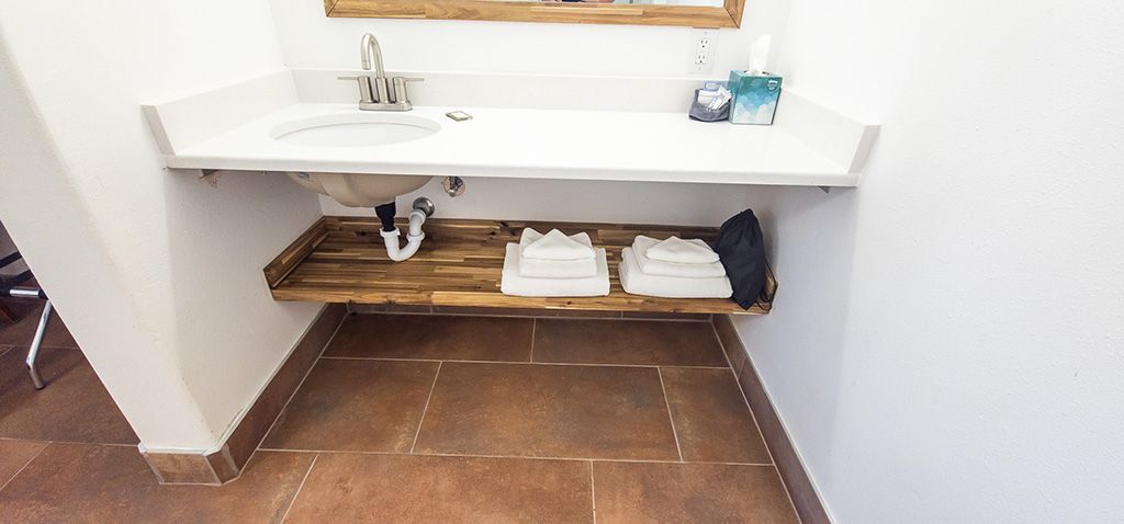 Small wall-mounted sink above a wooden shelf with folded towels in a restroom.