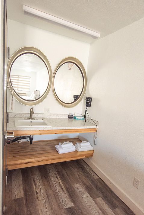 Small bathroom vanity with two round mirrors, white sink, wooden counter, and dark wood floor.
