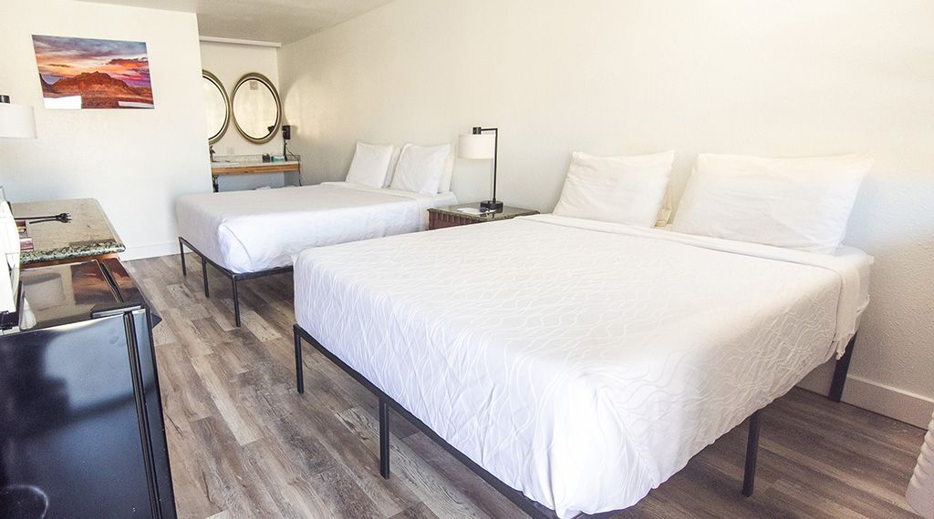 Bright bedroom with two white beds, a mirrored vanity, and gray wood flooring
