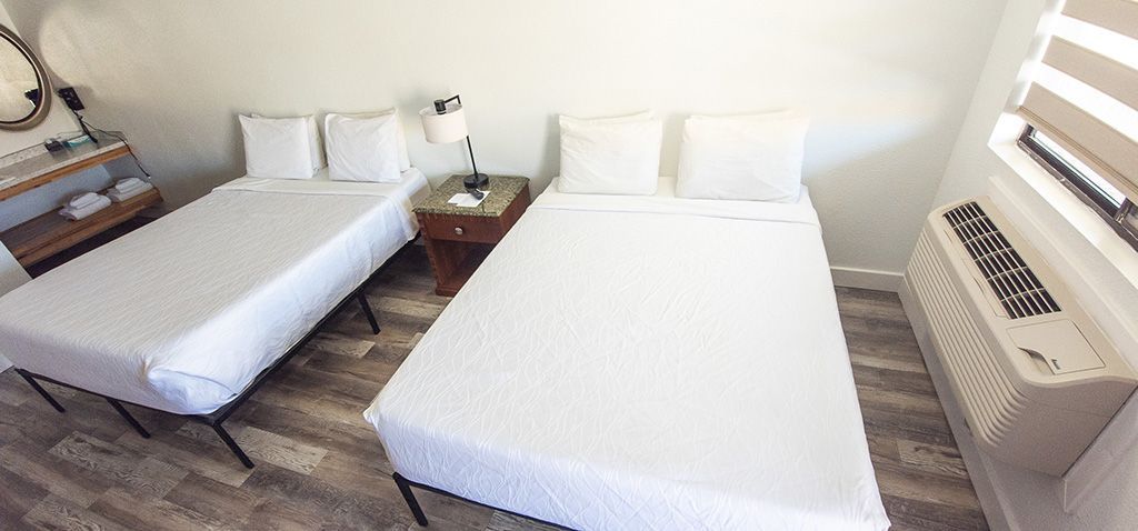 Bedroom with two white beds, bedside table, and window air conditioner on the right