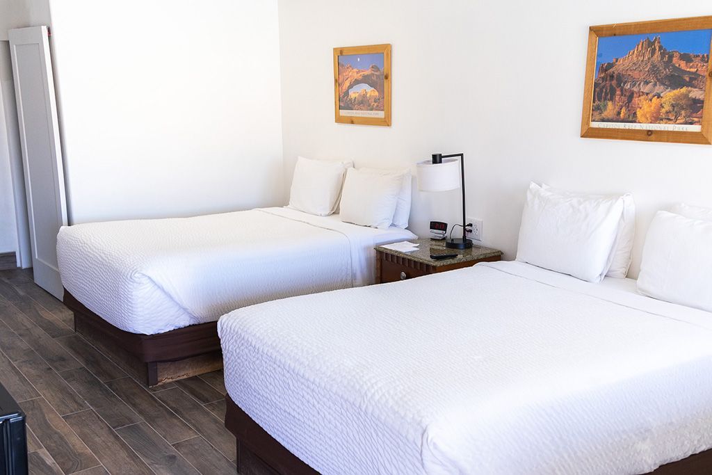 Bright hotel room with two white beds, dark wood floors, and framed wall art