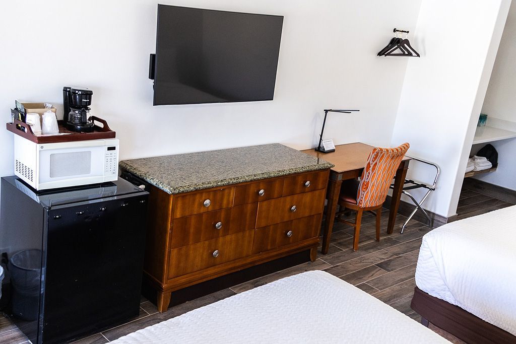 Bedroom with wall-mounted TV, wooden dresser, chair, desk, and bed in a compact room.