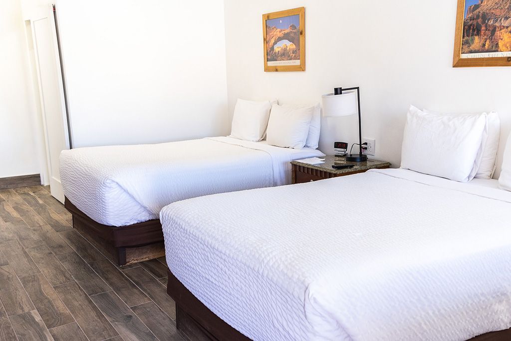 Bright bedroom with two white beds, wood floors, and framed wall art