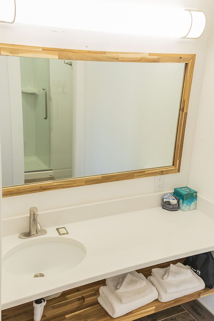 Bathroom vanity with white countertop, large mirror, sink, towels, and toiletries on the counter