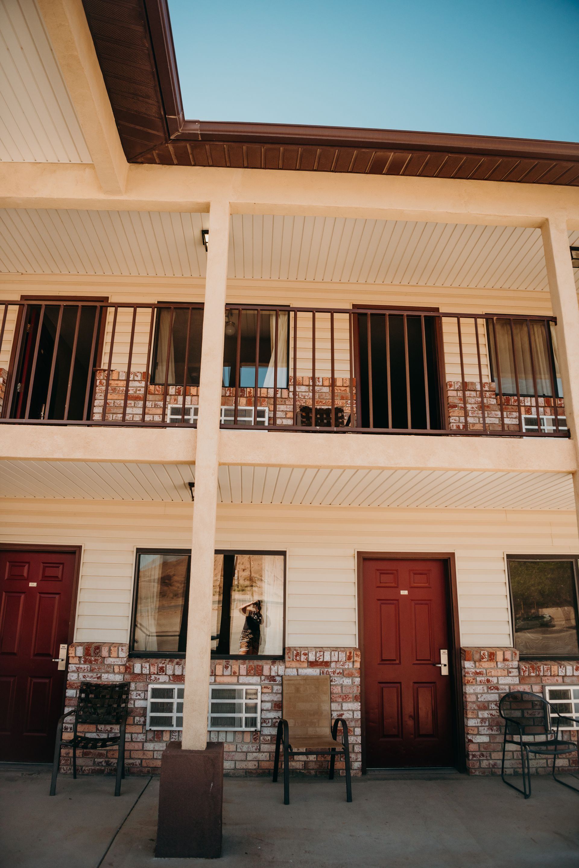 Two-story beige building with balconies, red doors, and chairs on the front porch