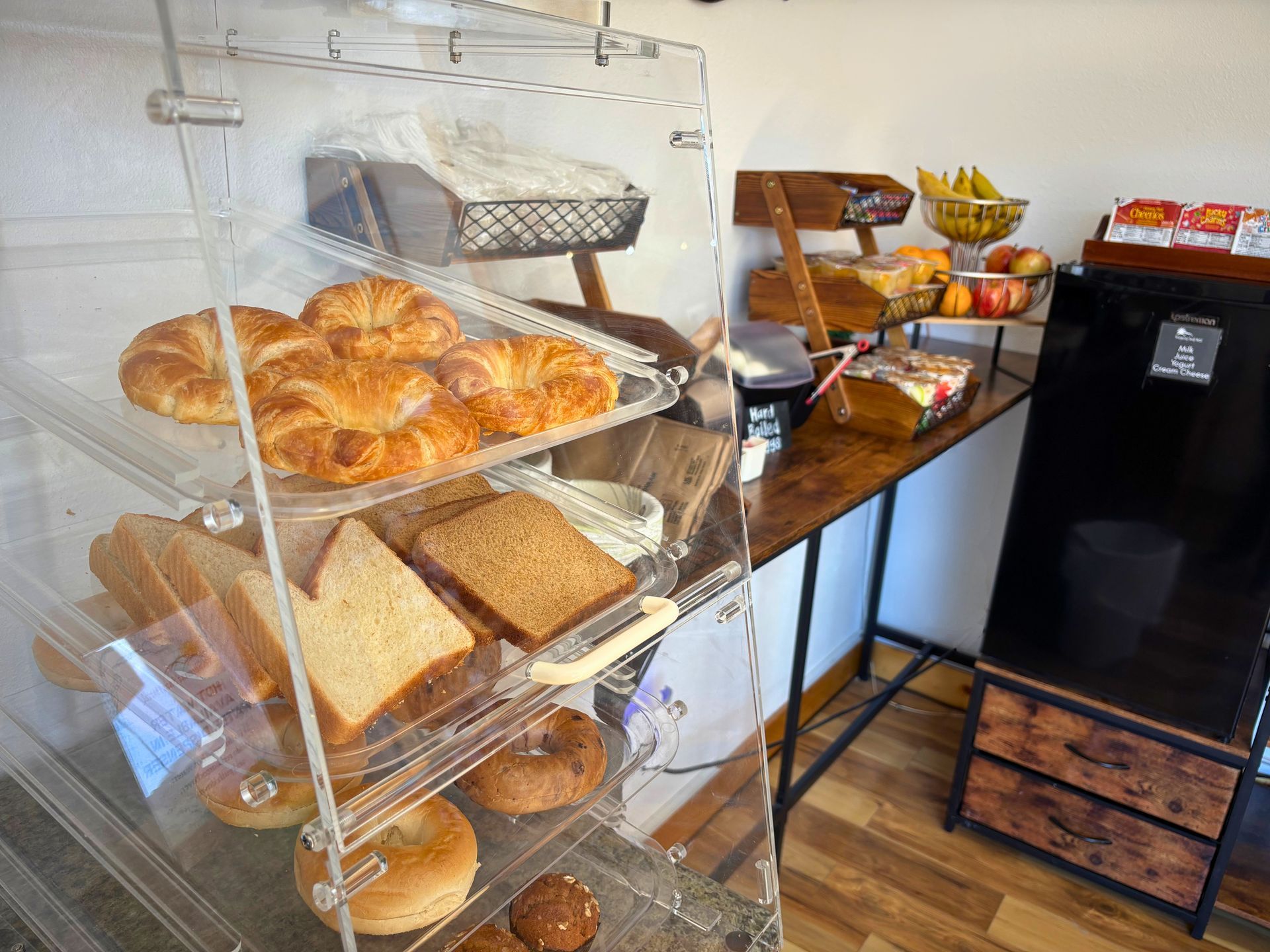 Bakery display case with croissants, muffins, and pastries beside a coffee station