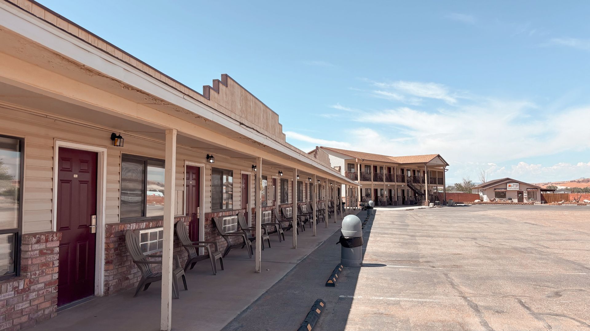 Sunlit street with adobe-style storefronts, porch columns, and a wide empty plaza under a blue sky