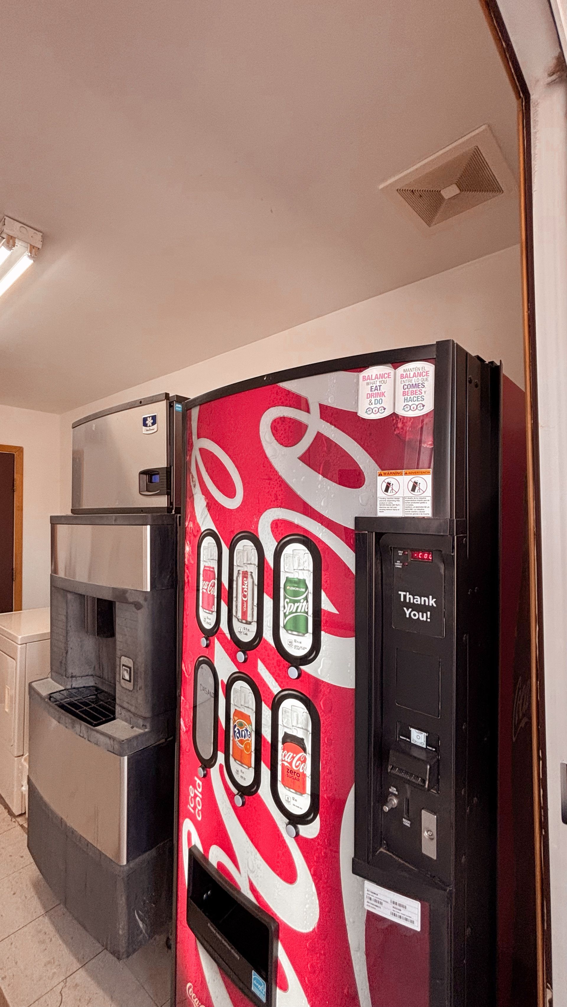 Coca-Cola vending machine beside a stainless steel microwave in a hallway or break room