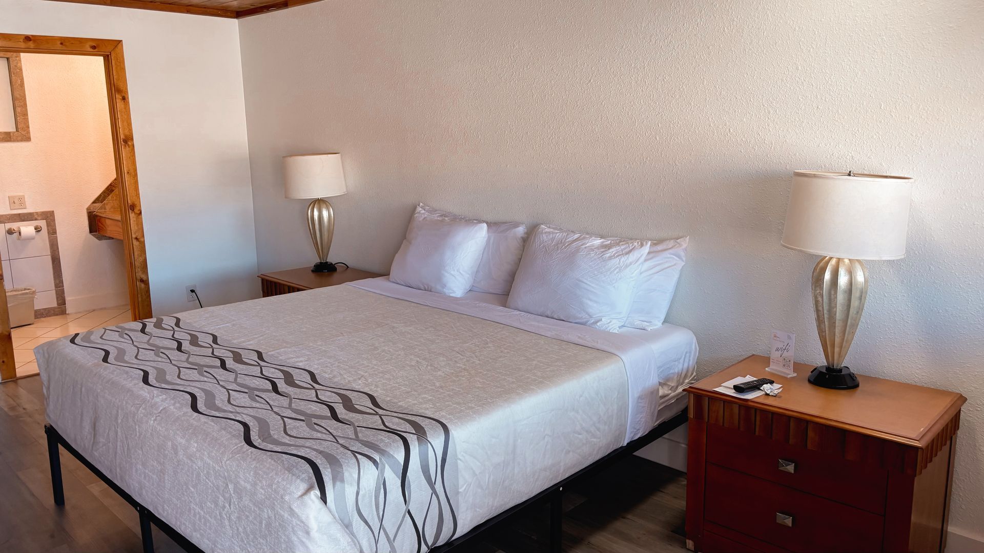 Hotel room with a large bed, bedside lamps, and a doorway to the bathroom.