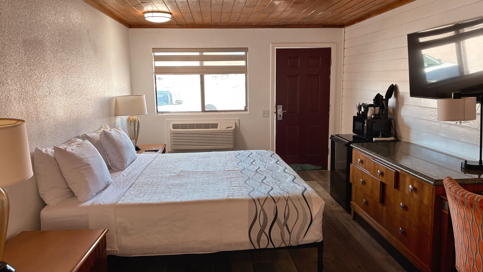 Small hotel room with two beds, wooden dresser, window AC, and TV.