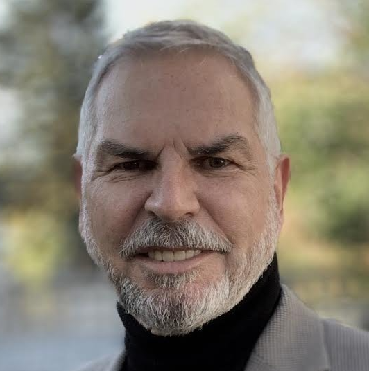 A man with a beard and a black turtleneck is smiling for the camera.