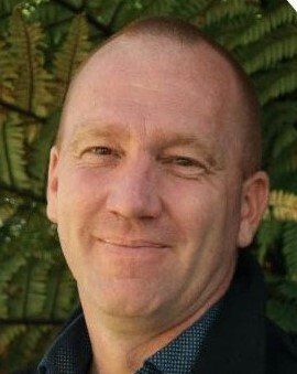 A close up of a man 's face with a fern in the background.