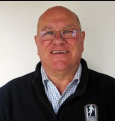 A bald man wearing glasses and a black jacket is smiling