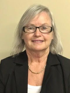 A woman wearing glasses and a black jacket is smiling for the camera.