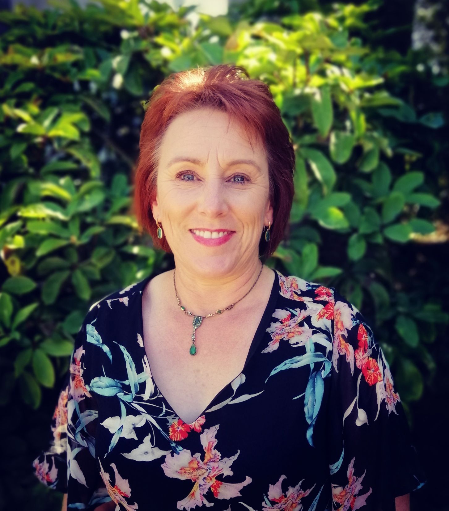 A woman wearing a floral shirt and a necklace smiles for the camera