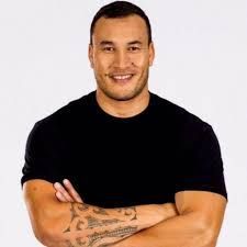 A man with a tattoo on his arm is standing with his arms crossed and smiling.