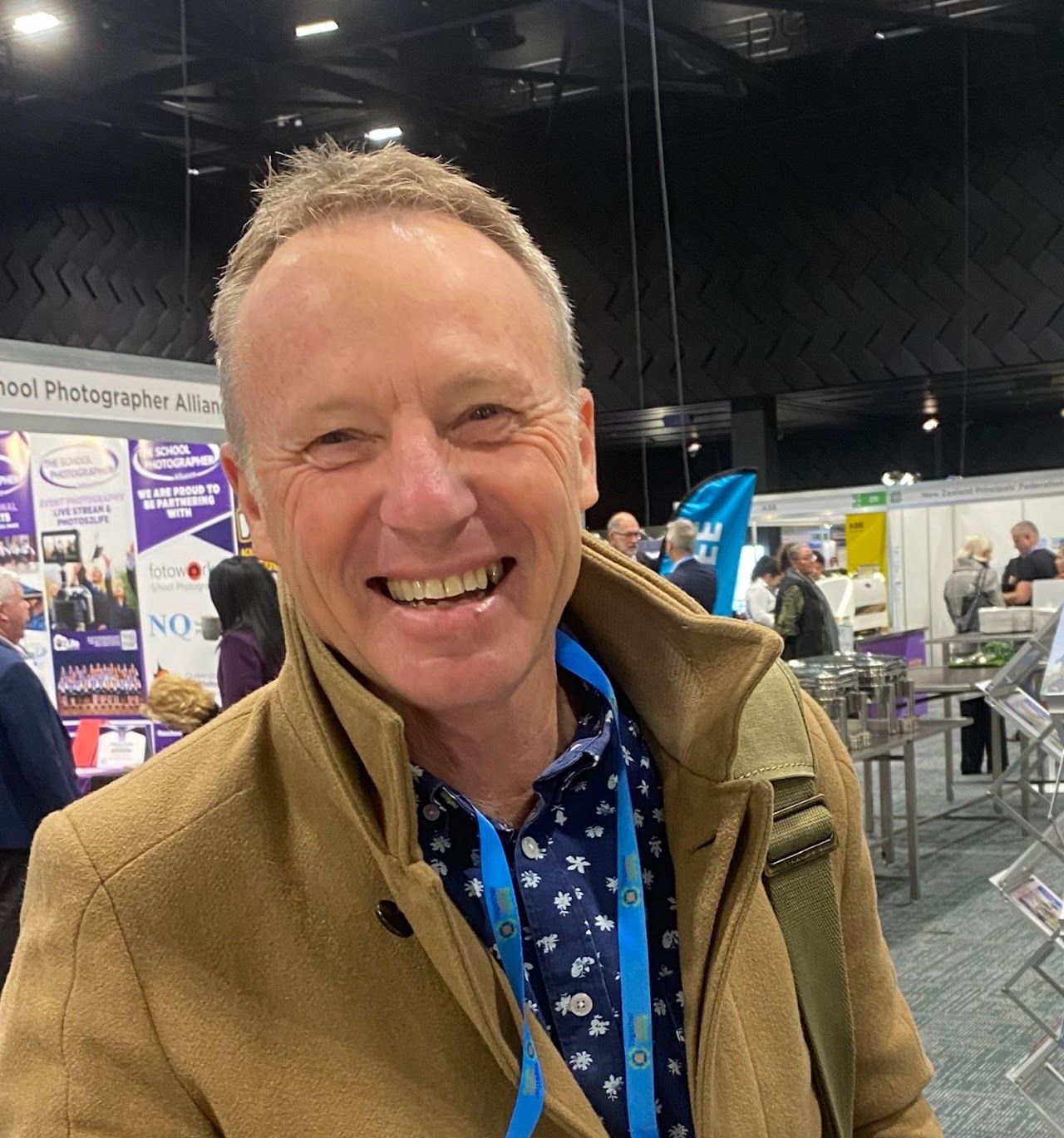 A man is smiling in front of a wall with pictures on it