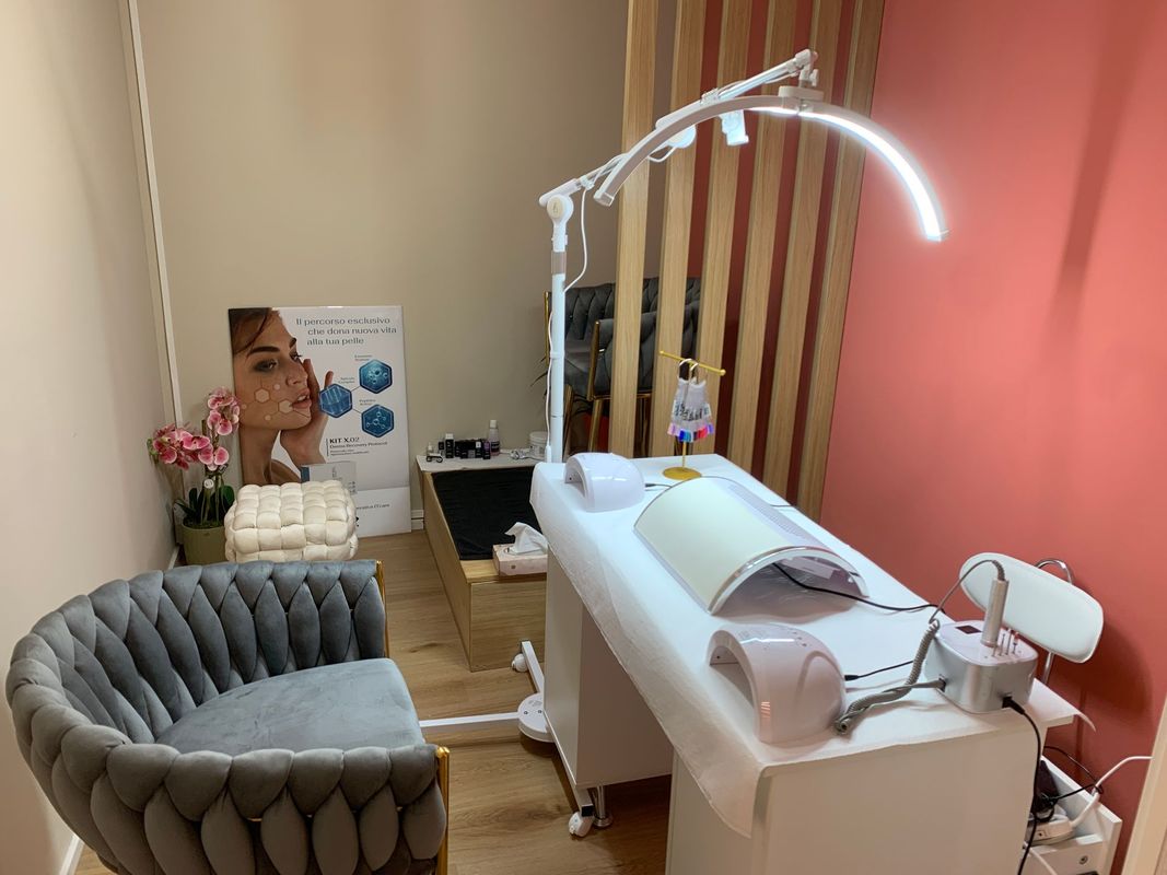 Cabina per trattamenti estetici con lettino per il viso, poltrona grigia, lampada e strumenti per la cura della pelle.