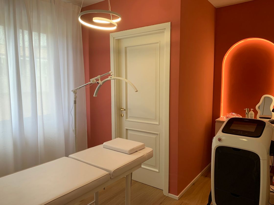 Sala trattamenti spa con lettino da massaggio, lampada a soffitto e pareti color corallo con alcova illuminata.