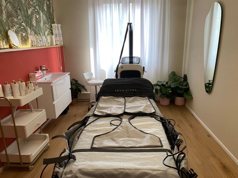 Sala massaggi con lettino da massaggio nero, parete con dettagli rossi, piante e specchio ovale.