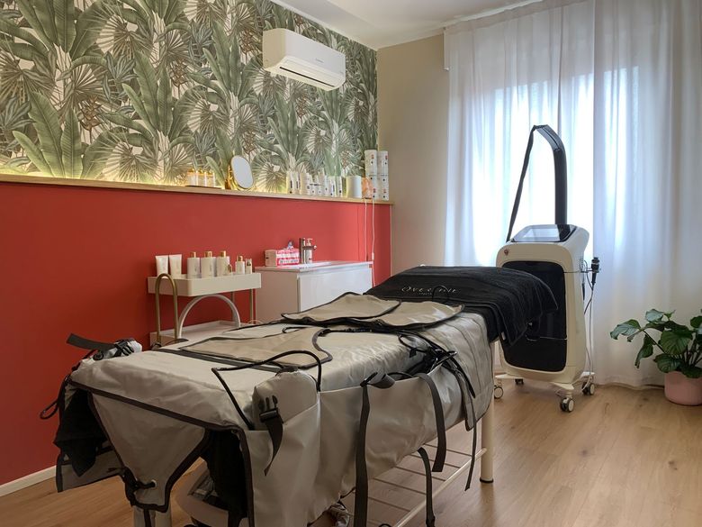 Sala trattamenti con lettino da massaggio e apparecchio medico accanto a una parete con dettagli rossi.