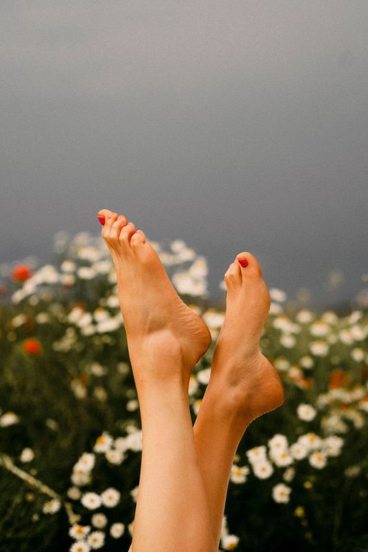 Piedi nudi sollevati sopra un campo di fiori bianchi contro un cielo grigio