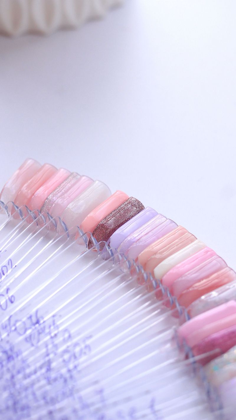 Primo piano di campioni di smalto per unghie artificiali rosa pastello e bianco disposti su una tavolozza a ventaglio trasparente.