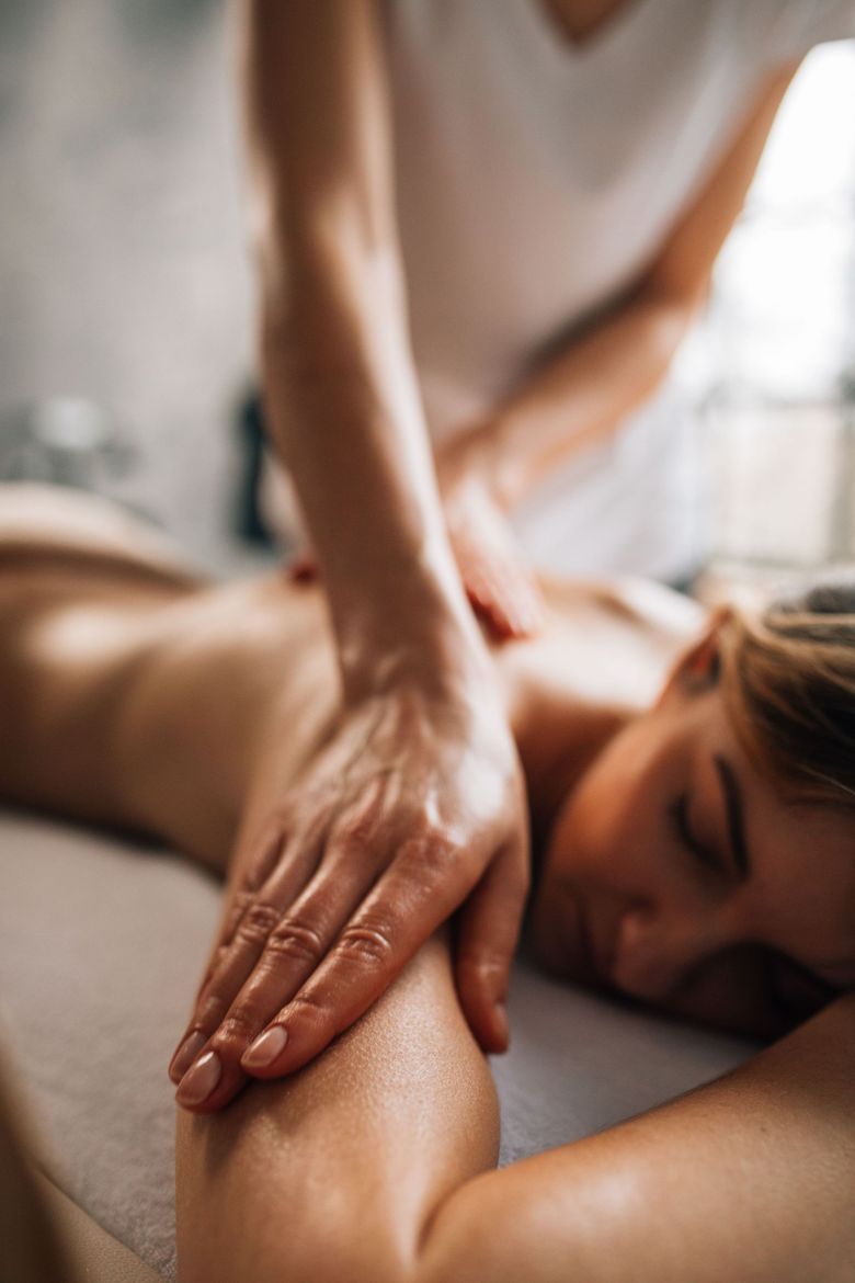 Una massaggiatrice preme sulla schiena di un cliente in una spa, primo piano delle mani sulla pelle.