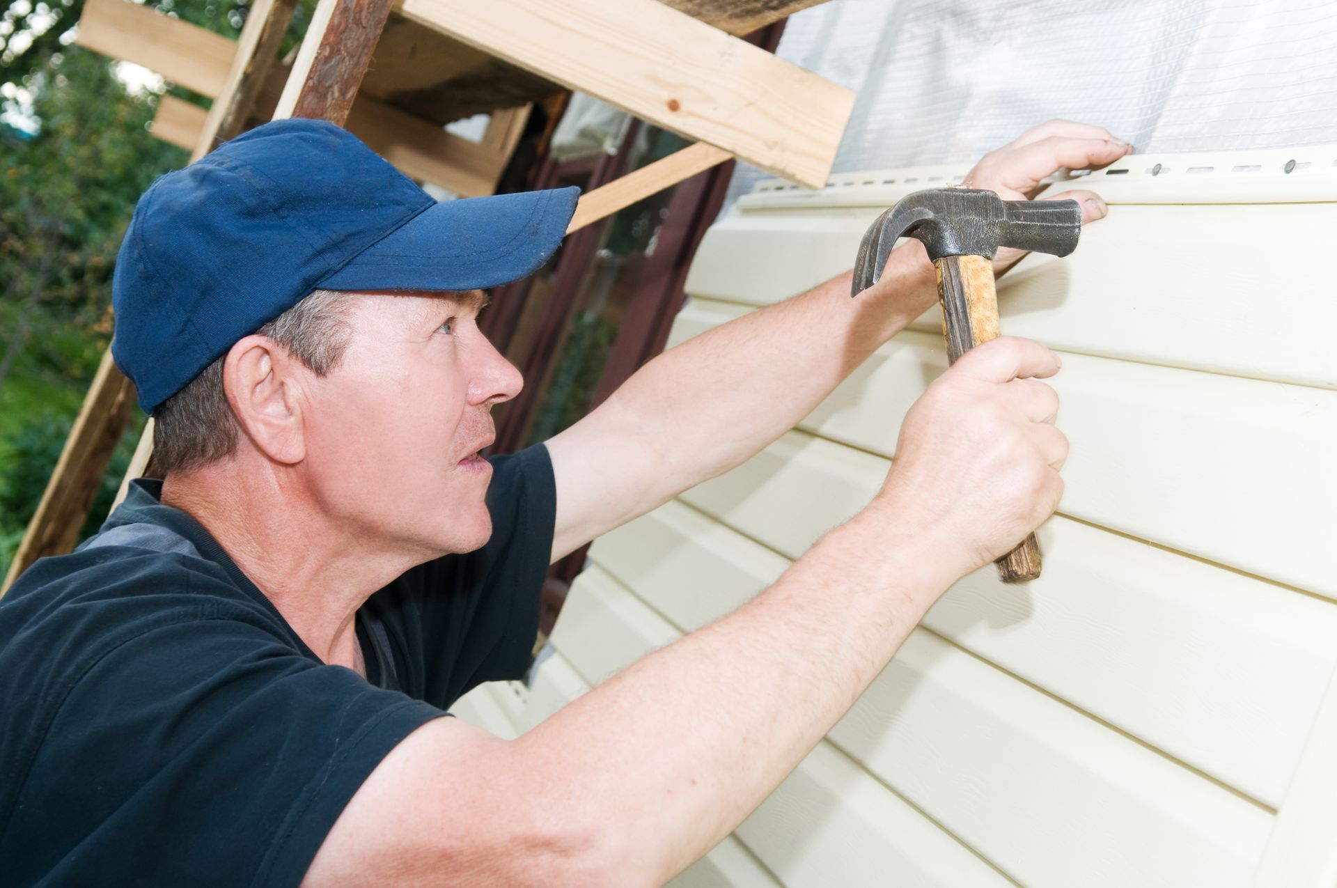 Man in blue cap hammering siding on a building's exterior. Man in blue cap hammering siding on a building's exterior.